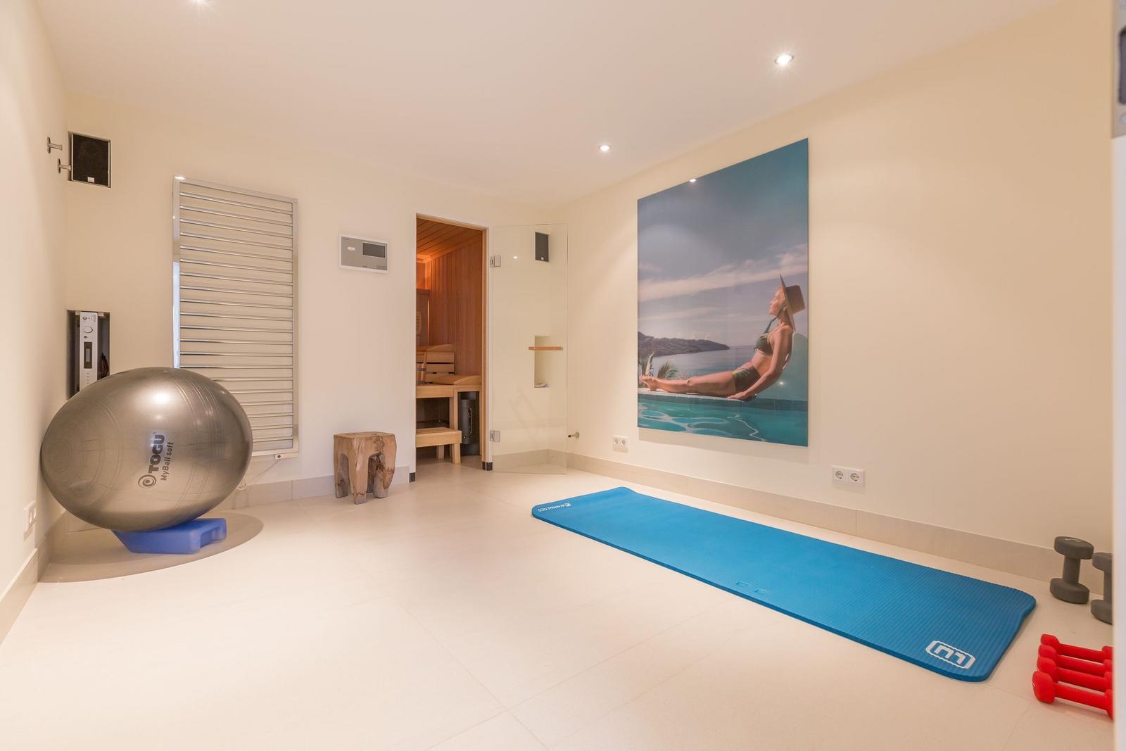 Fitness room with yoga mat, ball, and dumbbells. Sauna in background. Wall picture with pool motif.