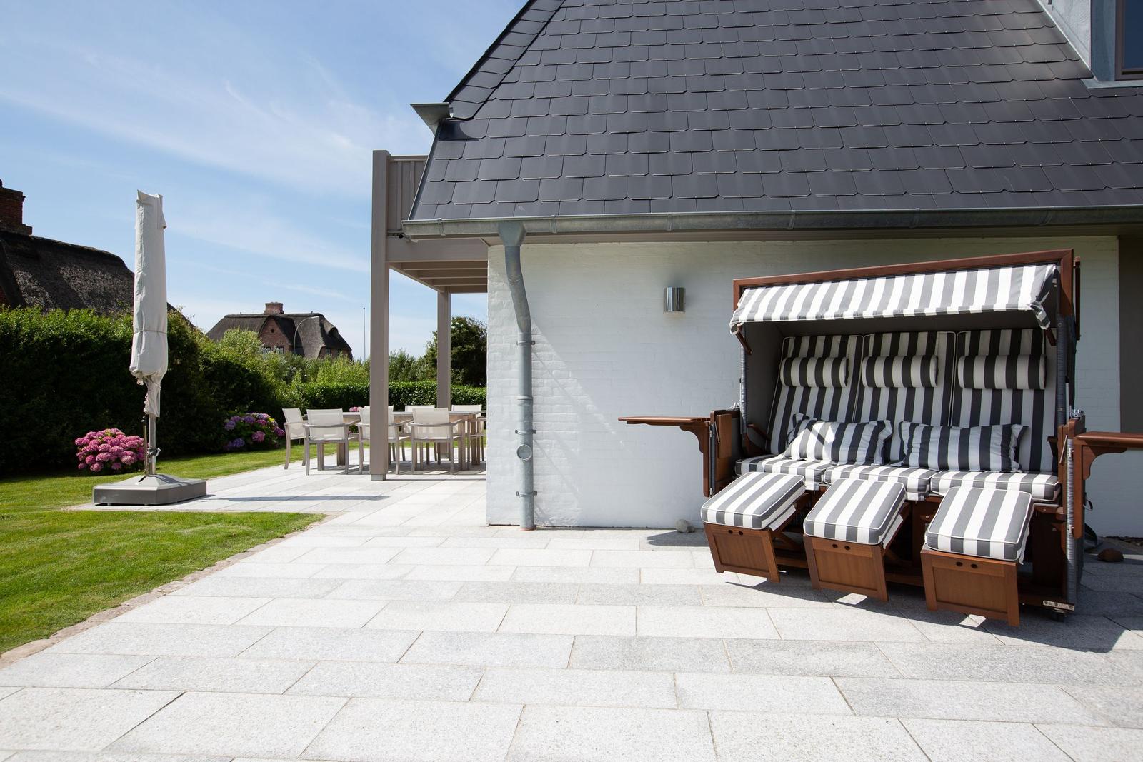 Terrace with beach lounger, table and chairs. Backyard with lawn and flowers.