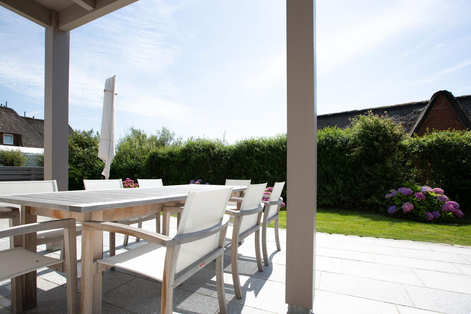 Terrace with table and chairs, surrounded by greenery and flowers.