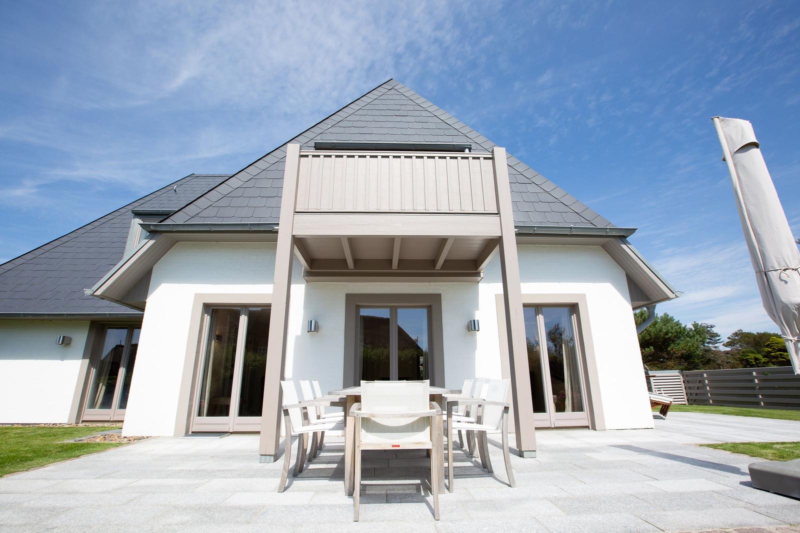 Modern villa with terrace and garden area under blue sky.