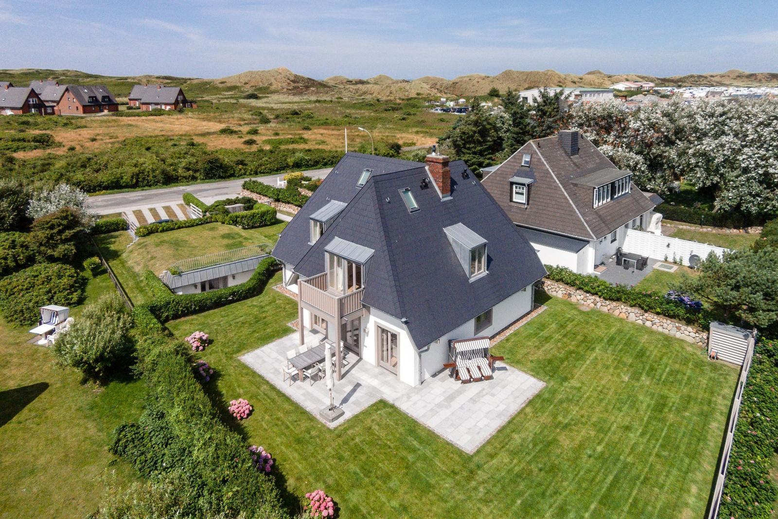 House with terrace and garden, surrounded by greenery and dunes.