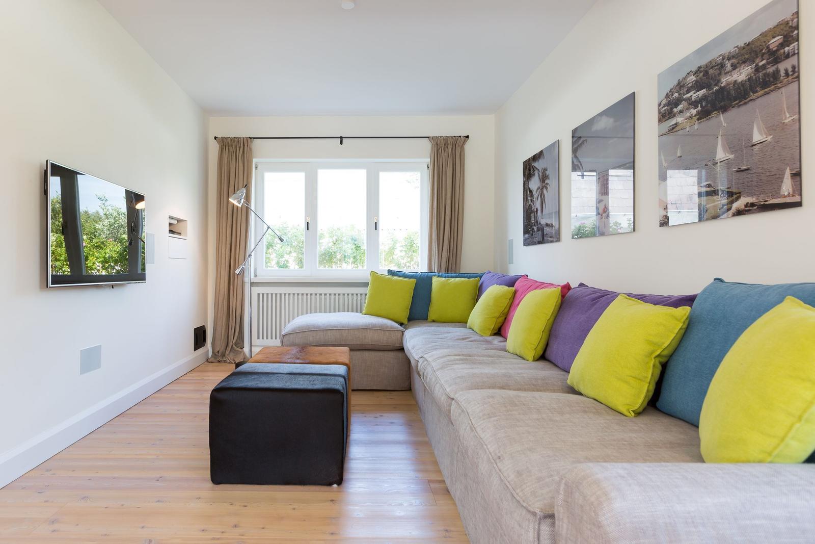 Living room with L-shaped sofa, colorful cushions, and TV mounted on wall.