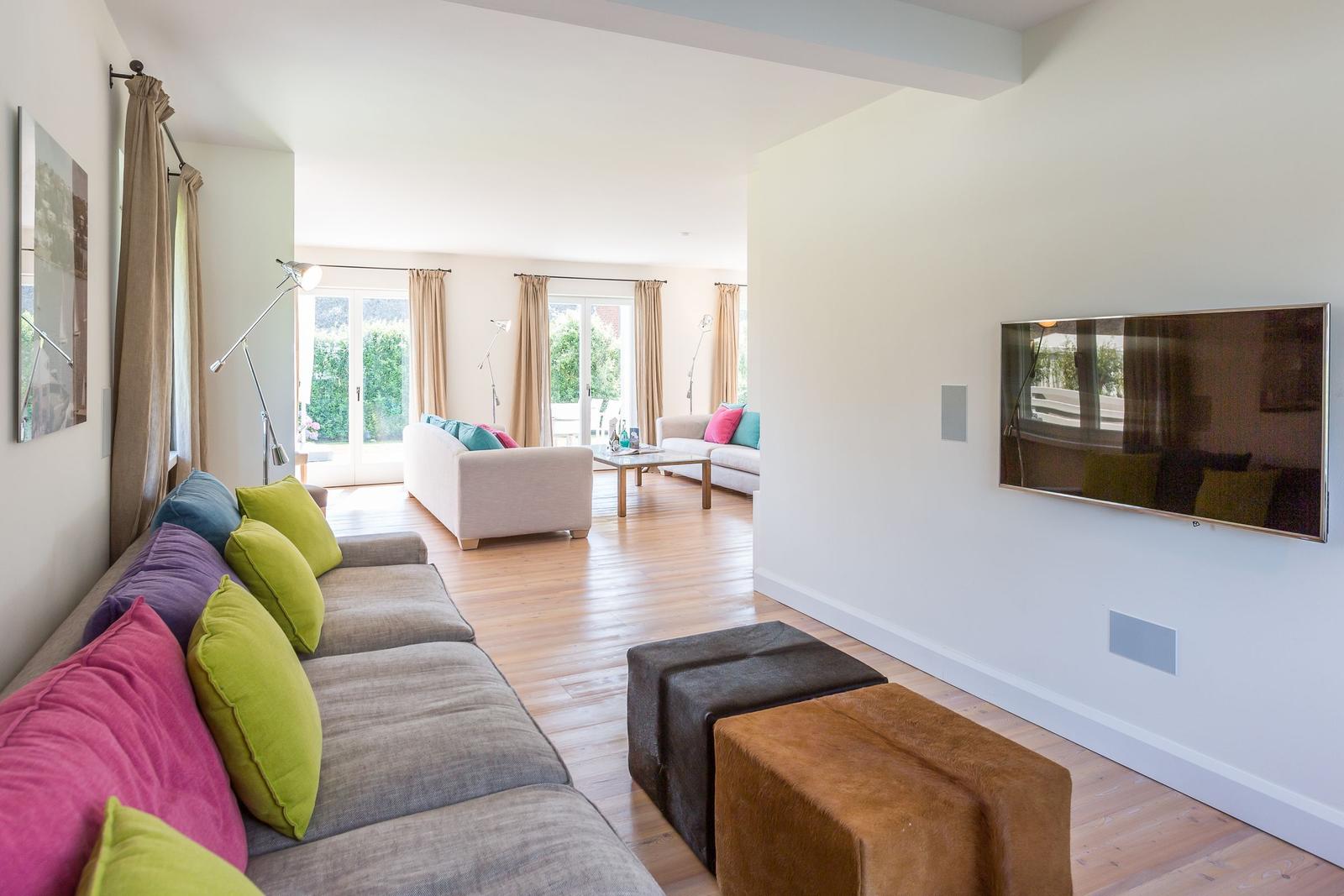 Living room with sofa, TV, and hardwood floor. Passage to balcony with seating area.