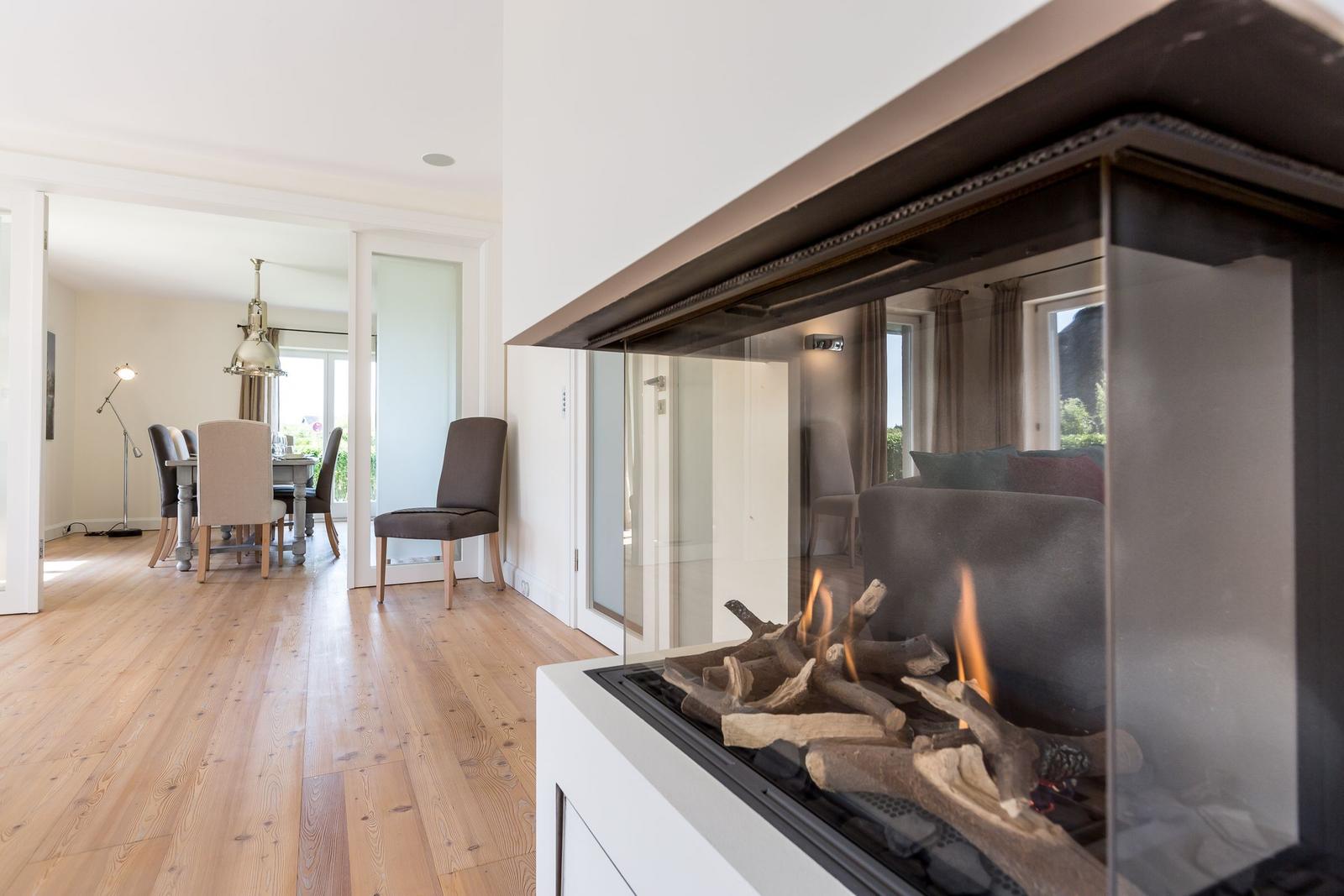 Fireplace with burning logs, adjacent living and dining area with wooden floor and furniture.