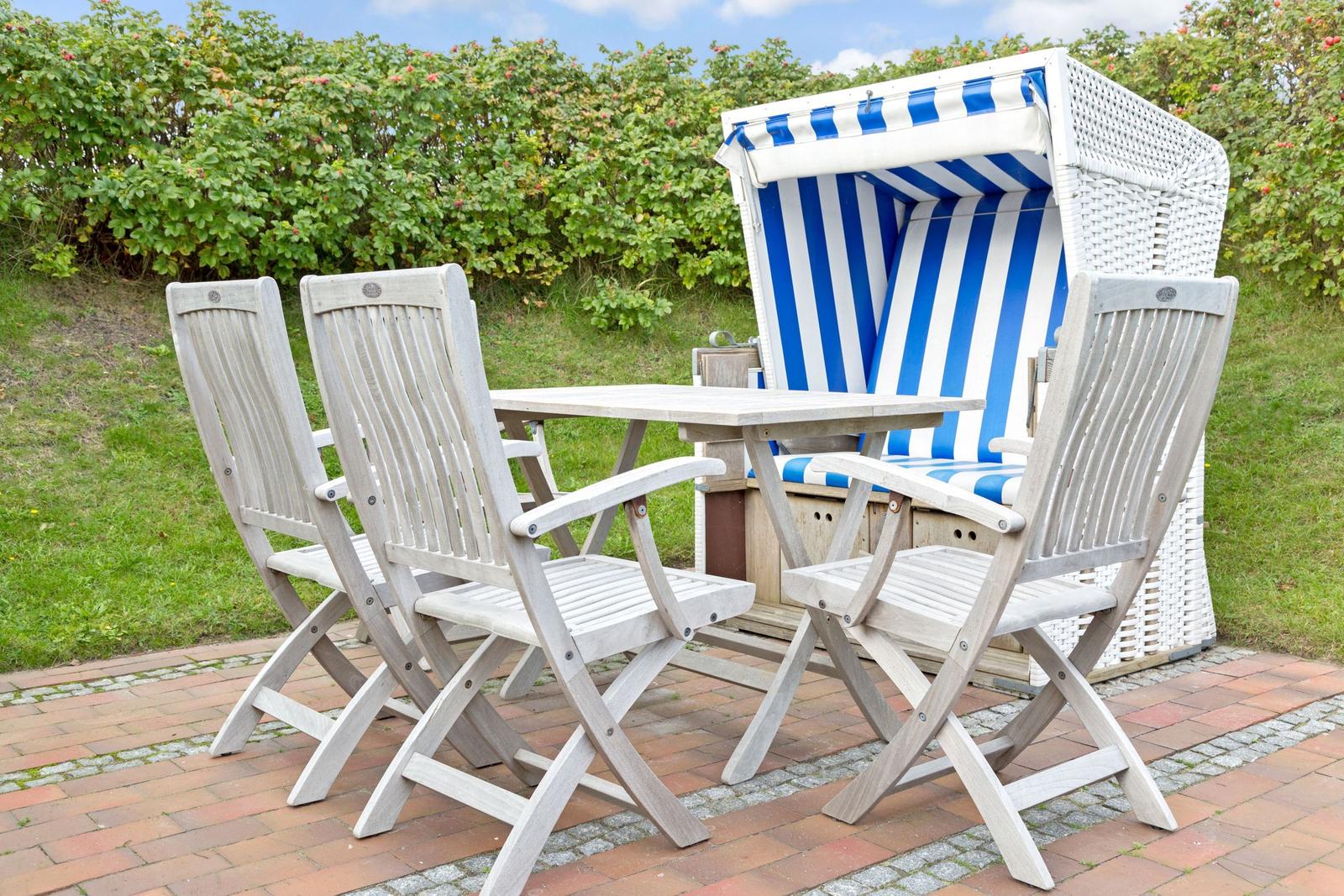Terrasse mit Tisch, vier Stühlen und Strandkorb mit blau-weißem Streifenmuster.