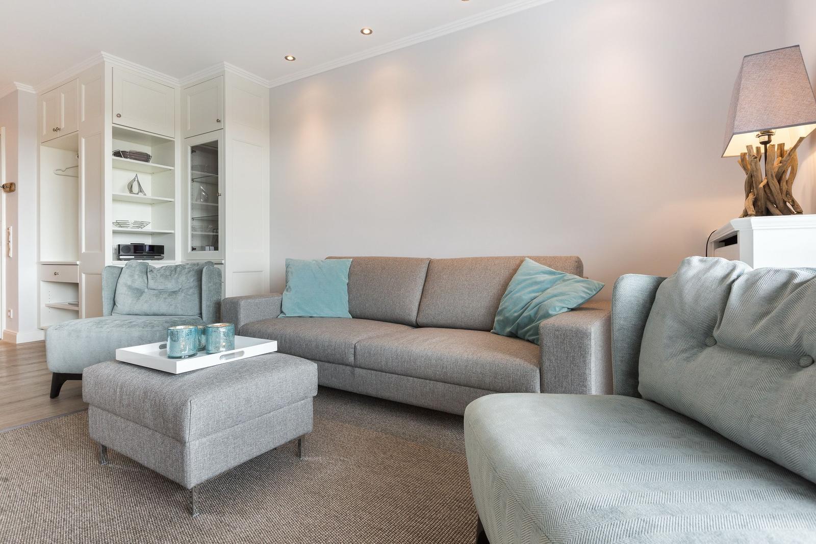 Living room with sofa, armchairs, and ottoman. Background: white cabinets.