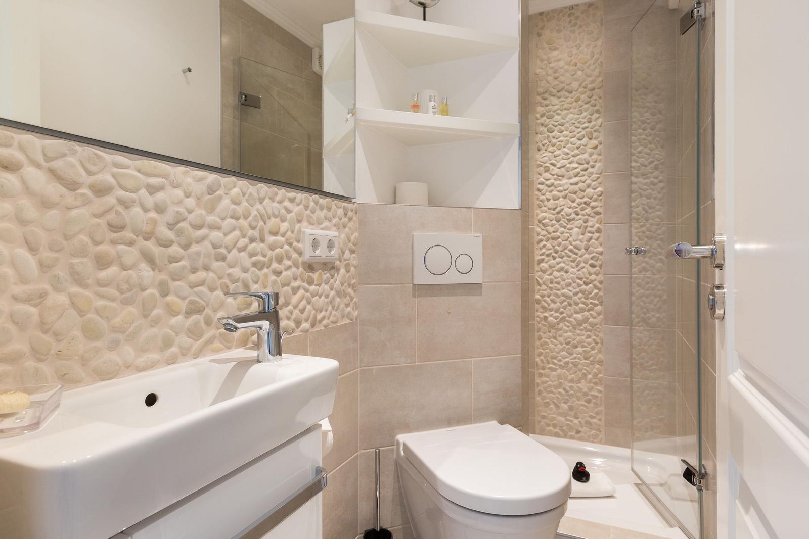 Bathroom with sink, toilet, and shower. Wall cladding made of stones.
