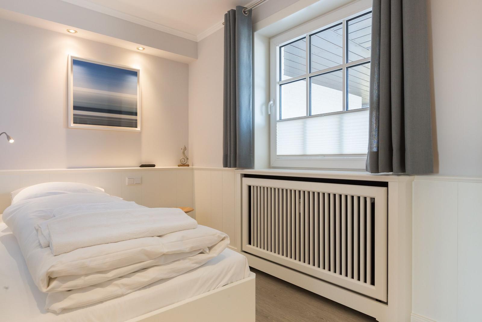 Bedroom with white bed, window, and radiator.
