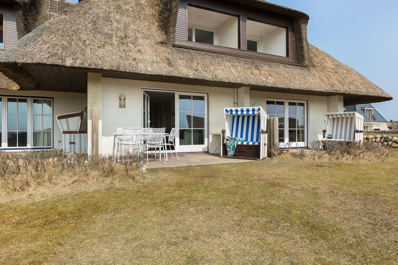 House with thatched roof, terrace, and beach chairs in the garden.