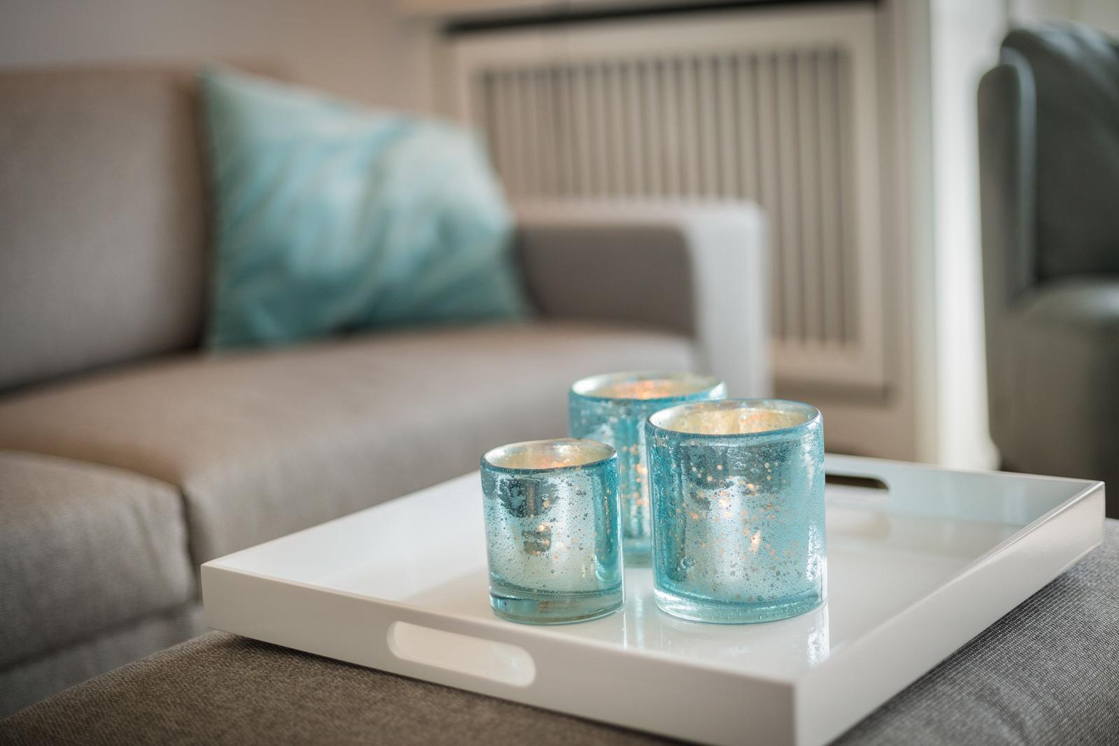 Three blue candle holders on a white tray in front of a sofa.