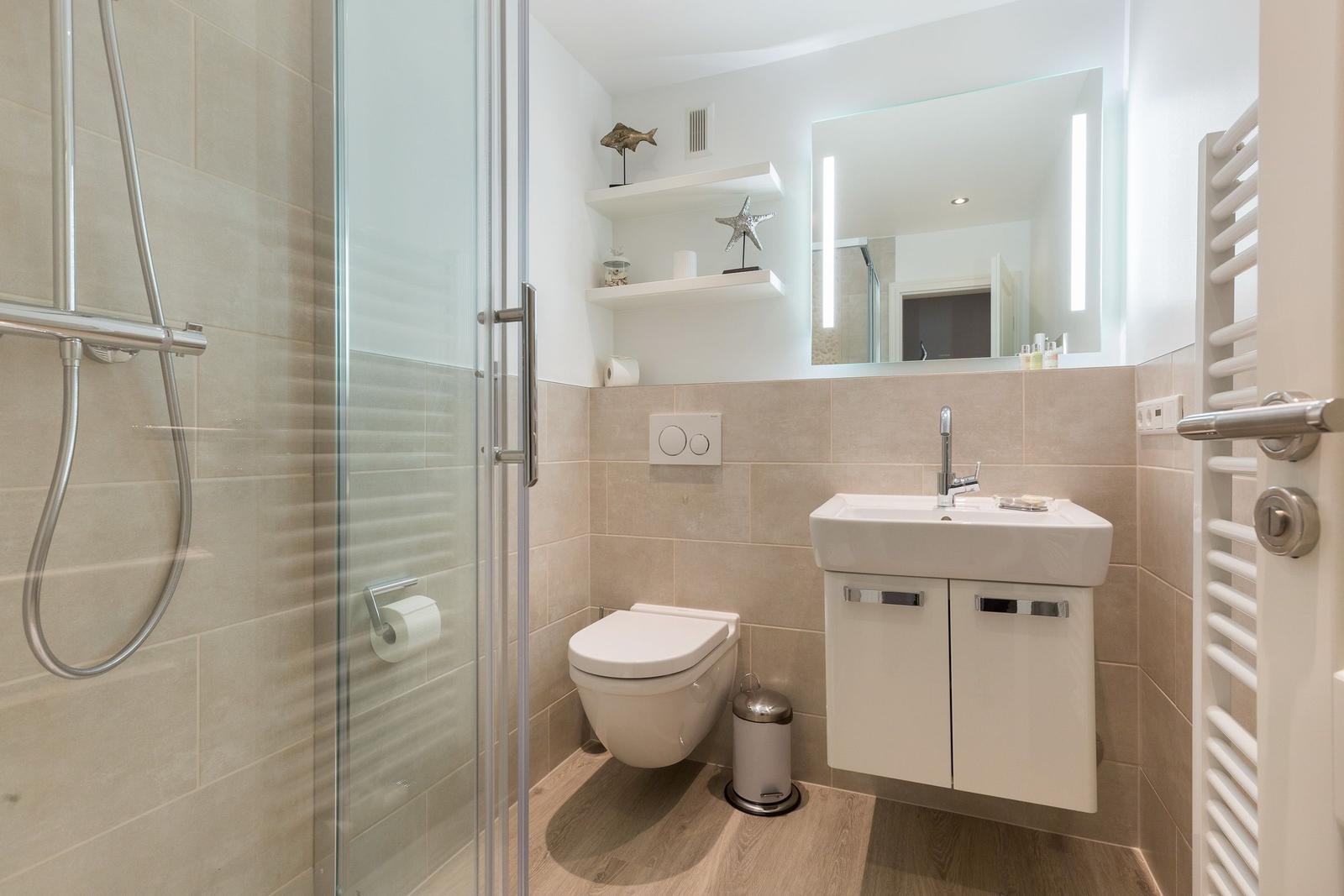 Bathroom with shower, sink, and toilet. Tiled wall and wooden floor.