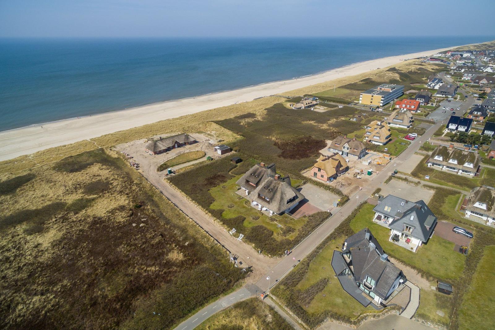 Aerial view of coastal village with thatched houses and sandy beach.