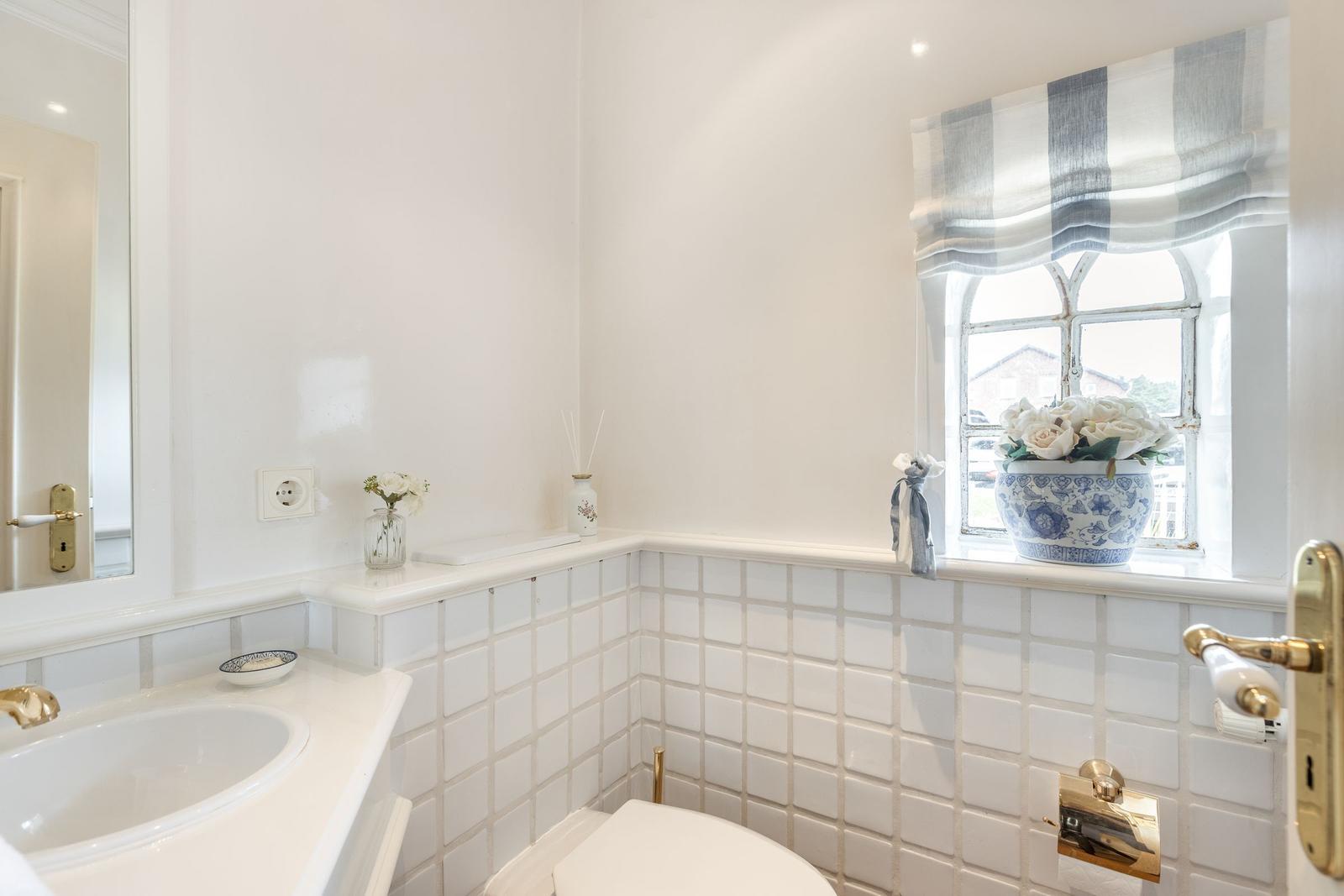 Badezimmer mit Waschbecken, Toilette und Fenster mit Blumen.