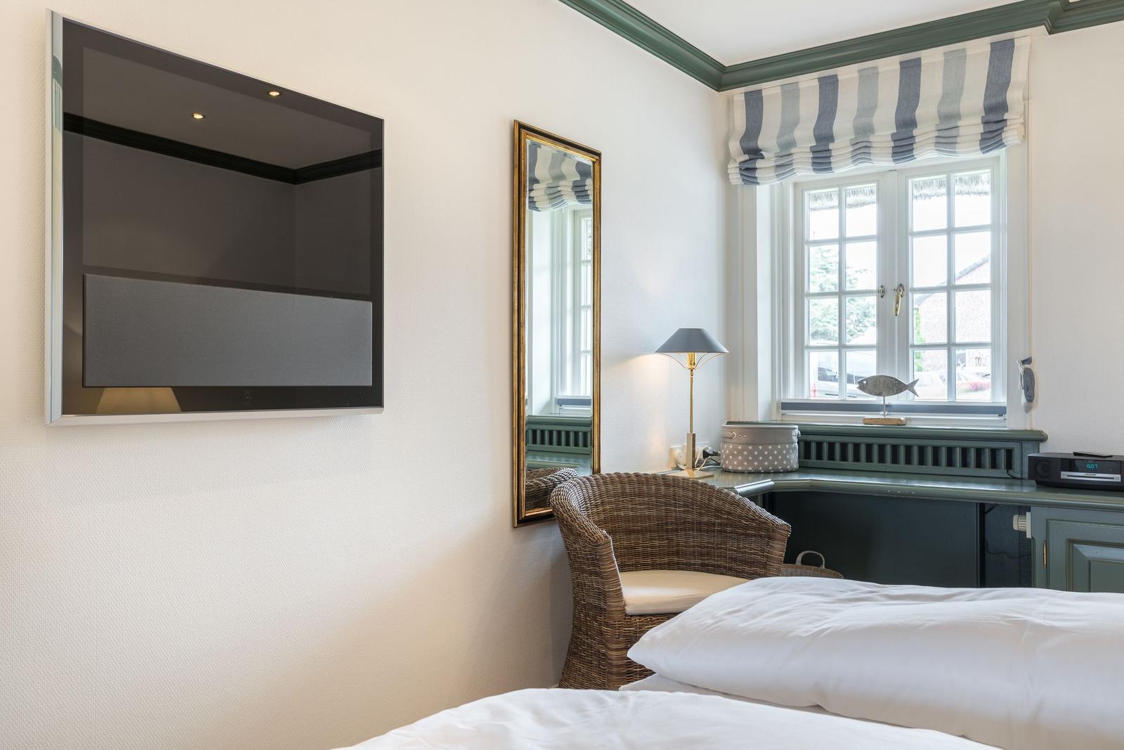 Zimmer mit Bett, Fernseher, Spiegel und Fenster mit Jalousie.