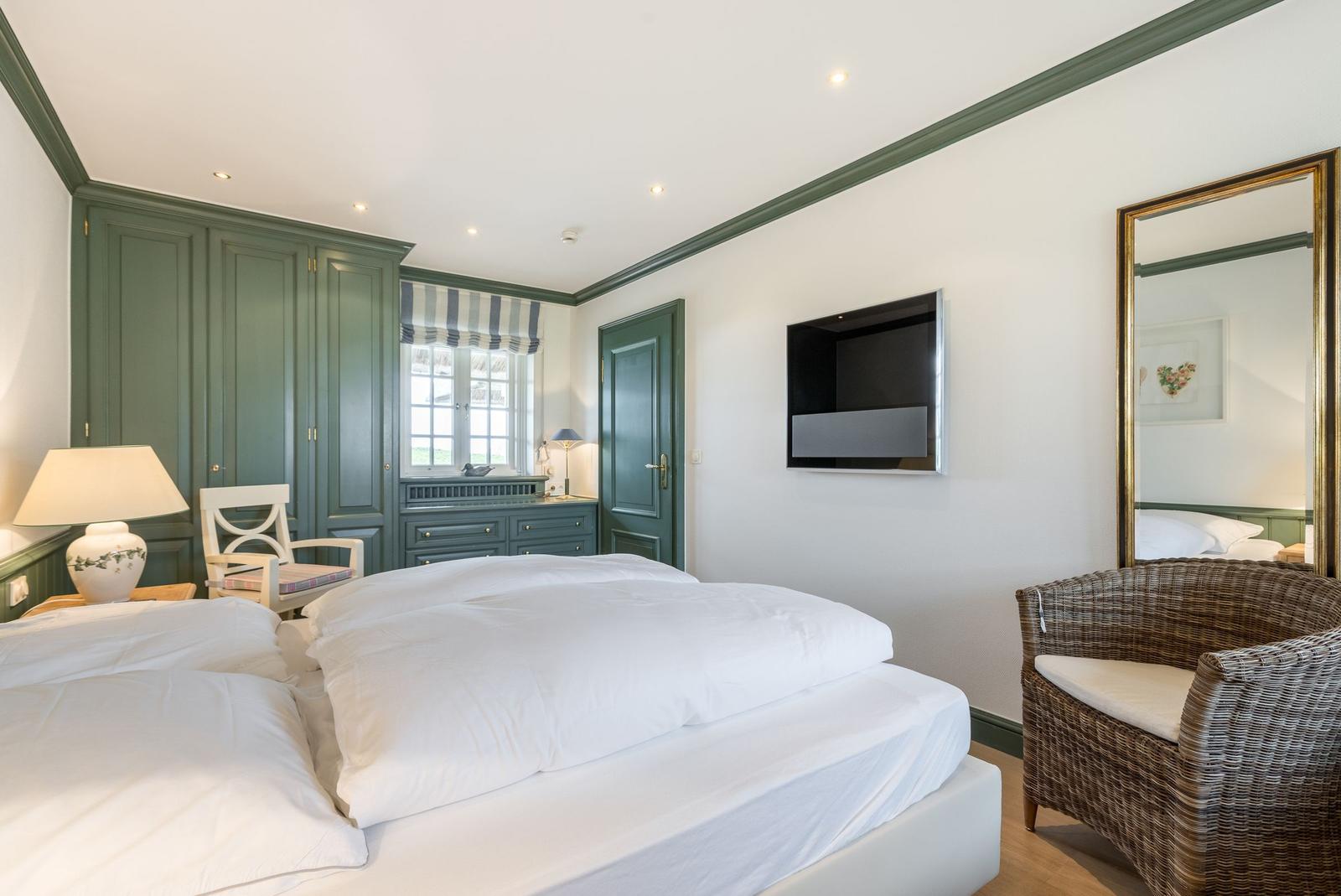 Schlafzimmer mit Bett, Kleiderschrank und Fernseher an der Wand.
