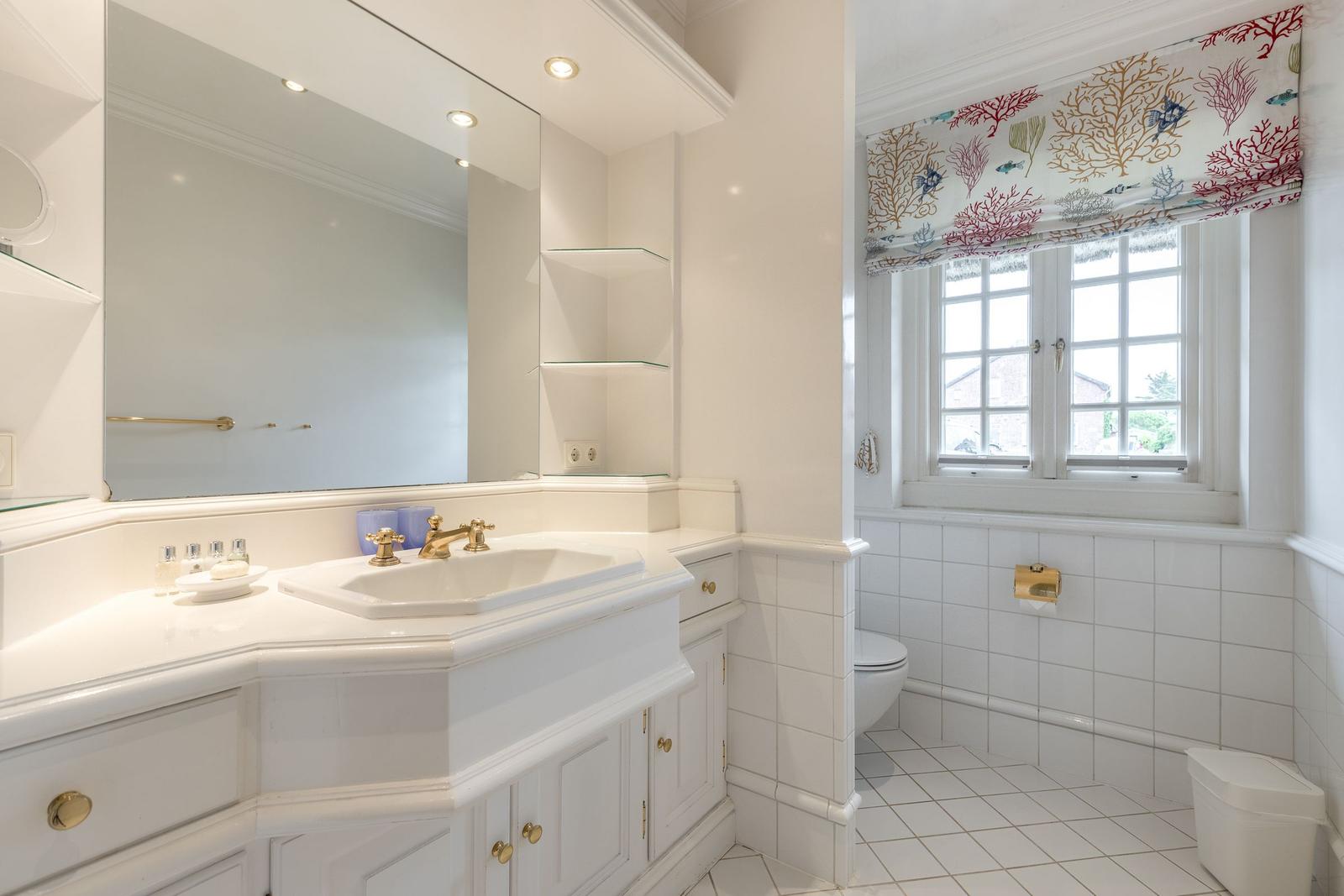 Badezimmer mit Waschbecken, Spiegel und Fenster mit Vorhang.