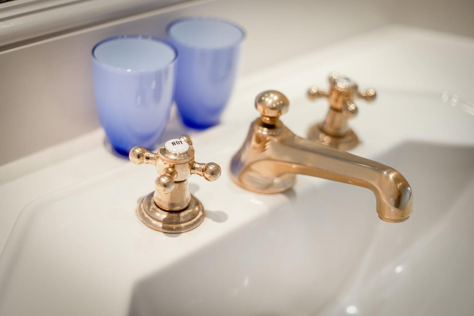 Waschbecken mit goldenen Wasserhähnen und zwei blauen Gläsern.
