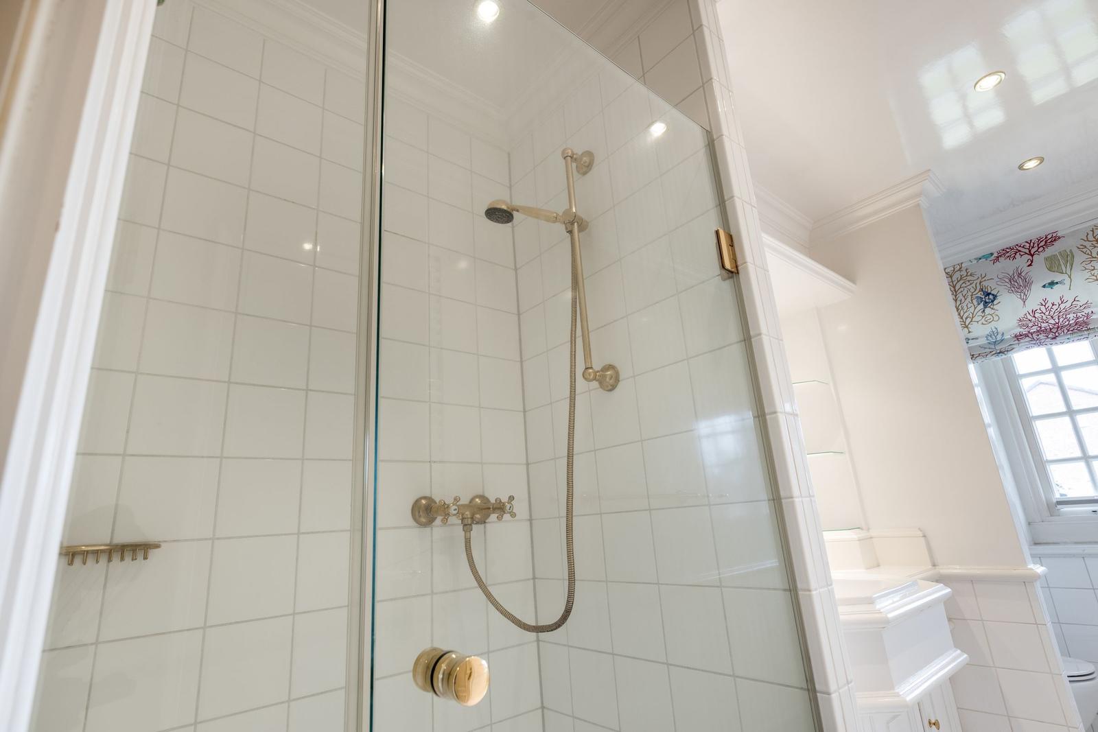 Dusche mit Glaswand, goldfarbenen Armaturen und weißen Fliesen.