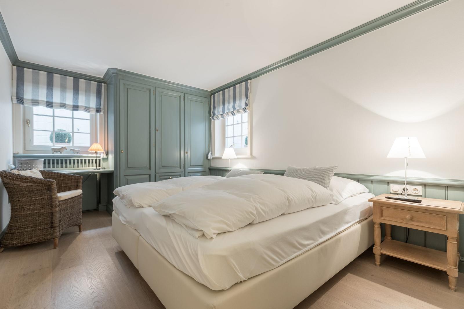 Schlafzimmer mit Bett, Nachttisch, Schrank und Fenstern mit Rollläden.