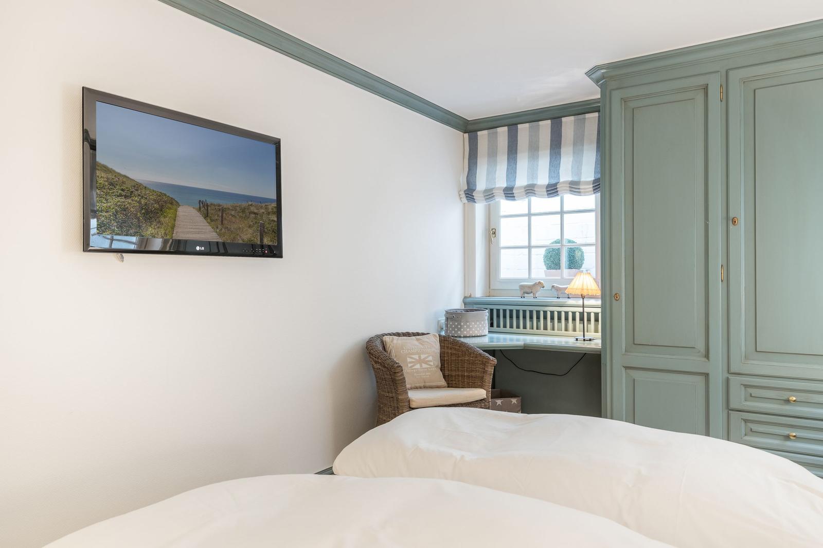 Schlafzimmer mit Bett, TV und Kleiderschrank. Fenster mit Streifenrollo.