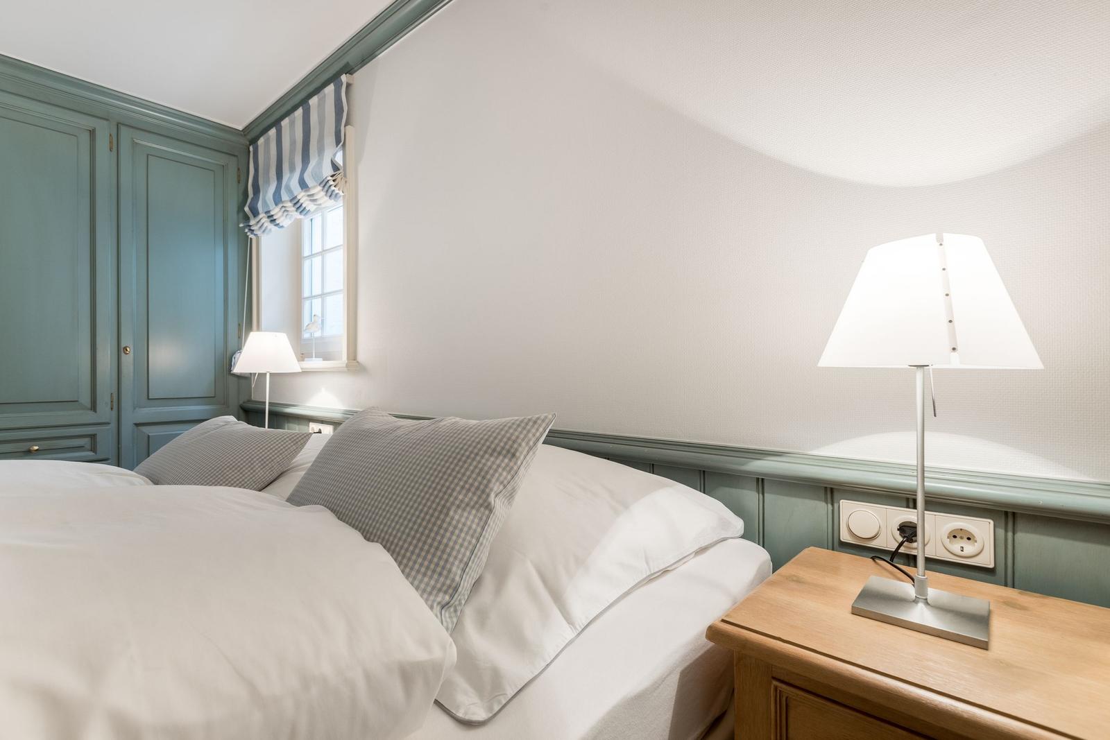 Schlafzimmer mit Bett, Nachttisch, Lampe und Kleiderschrank.
