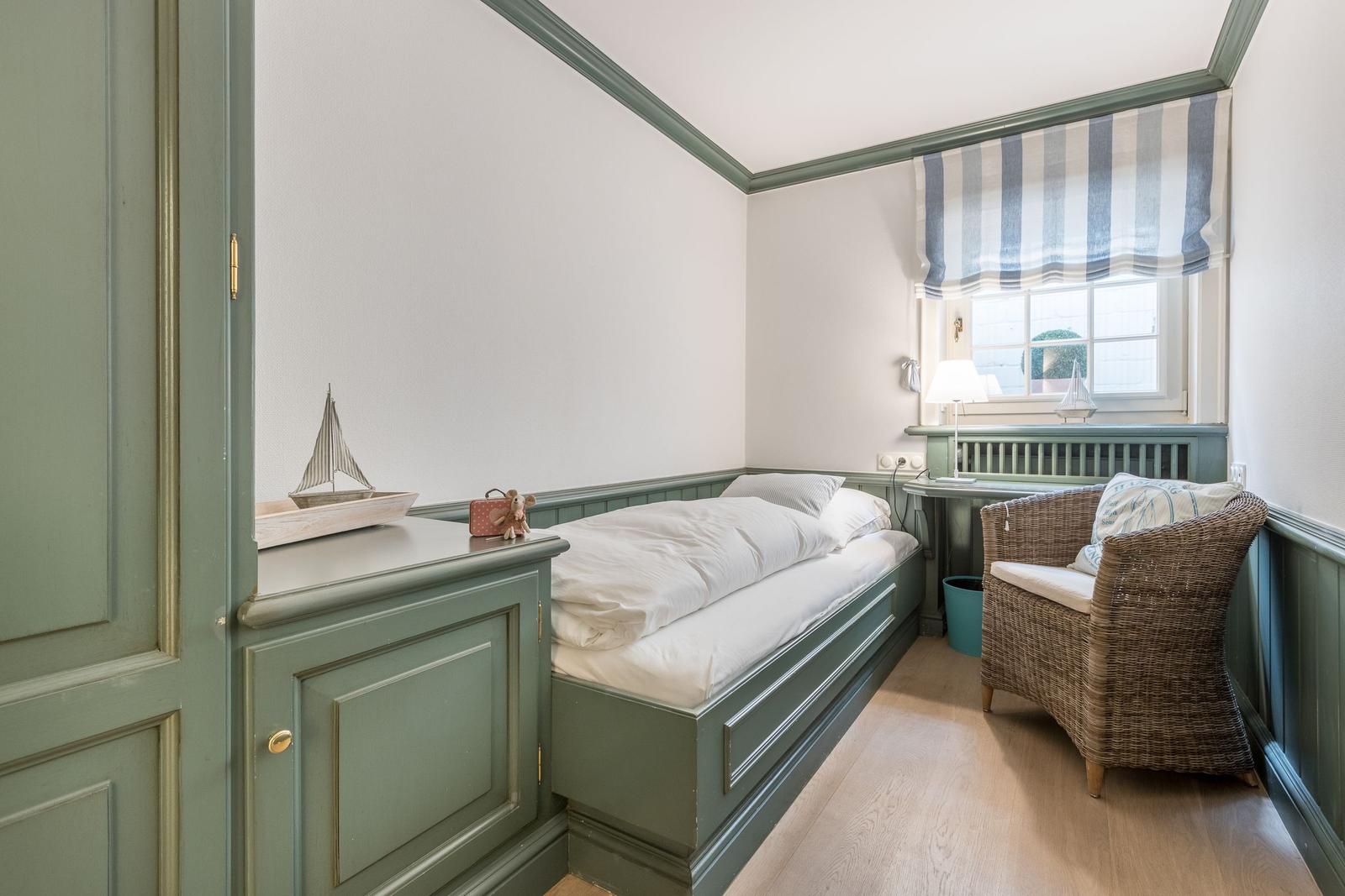 Ein Schlafzimmer mit Bett, Stuhl und Fenster mit Vorhang.