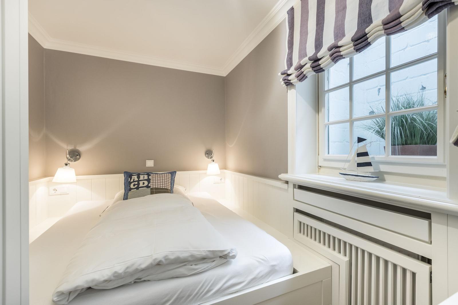 Schlafzimmer mit Bett, Nachttischlampen und Fenster mit Segelbootmodell.