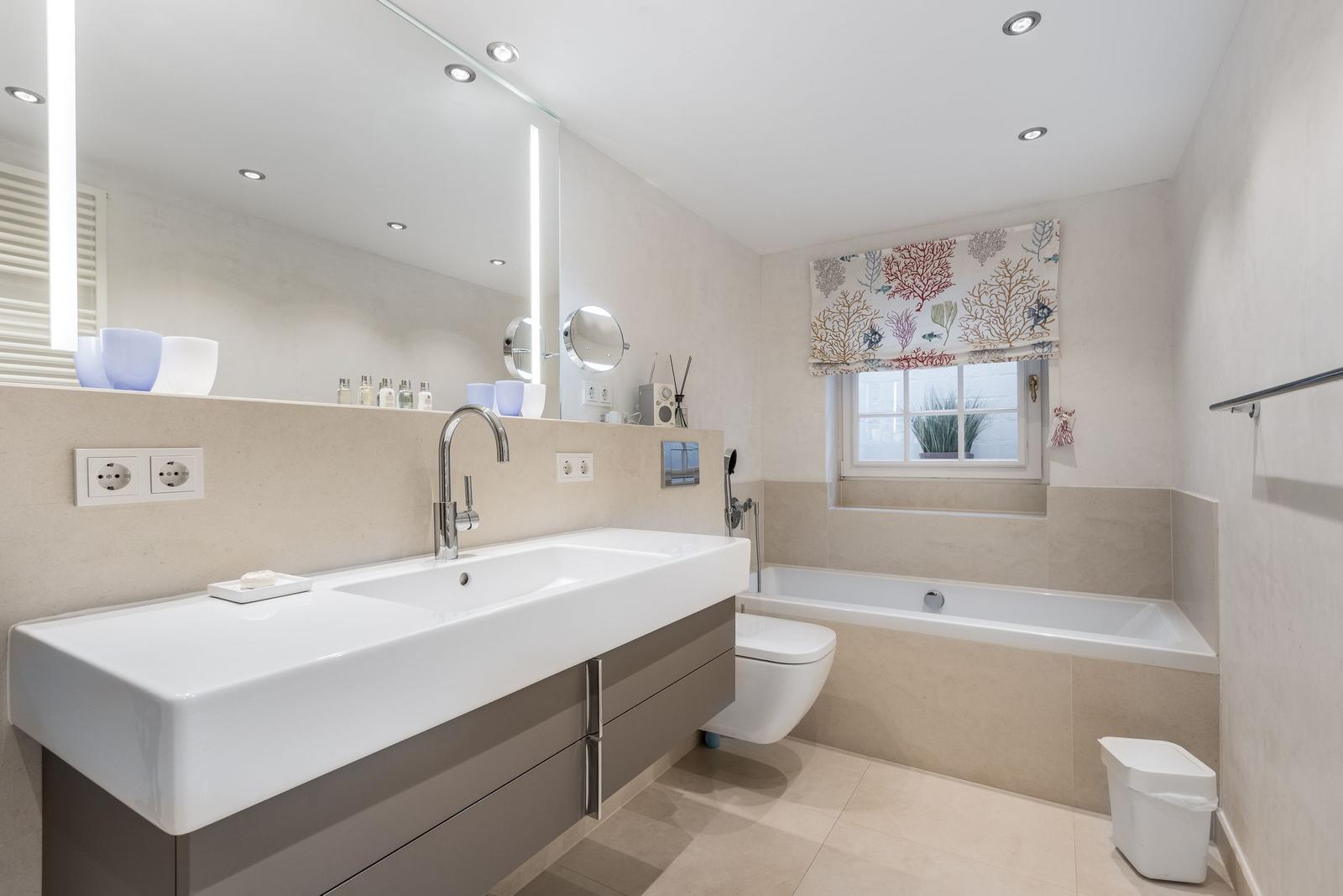 Bad mit Waschtisch, Badewanne und Toilette. Fenster mit Vorhang.