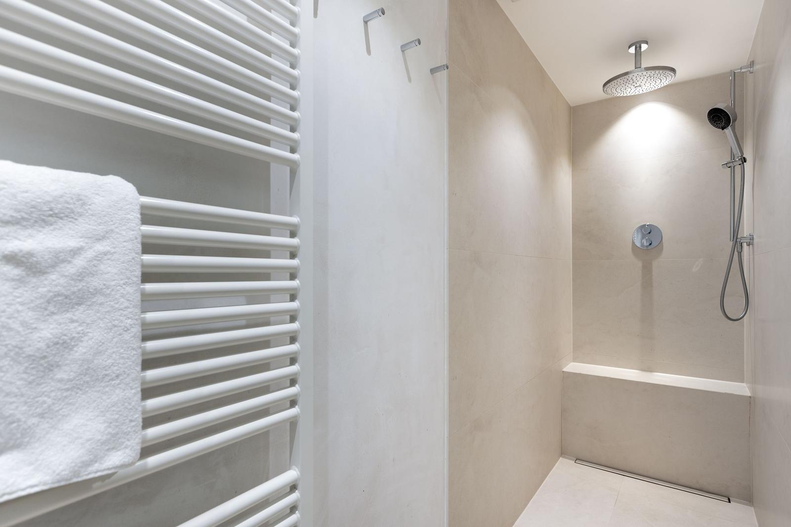 Dusche mit Duschbrause und Heizkörper mit Handtuch.