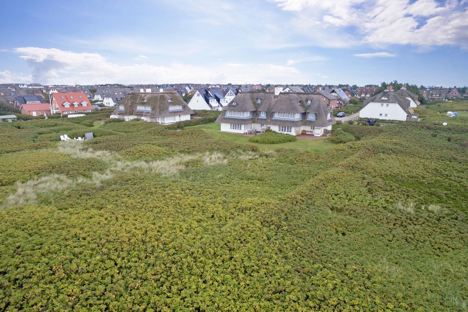 Dorfhäuser mit Strohdächern auf grüner Dünenlandschaft unter blauem Himmel.