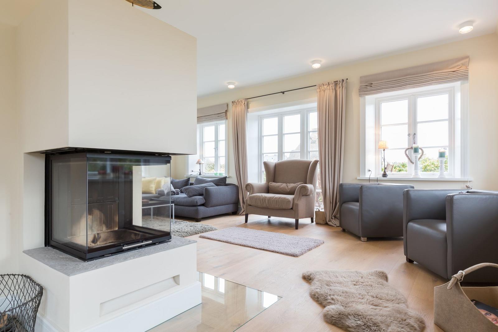 Wohnzimmer mit Kamin, Sitzgruppe und großen Fenstern.