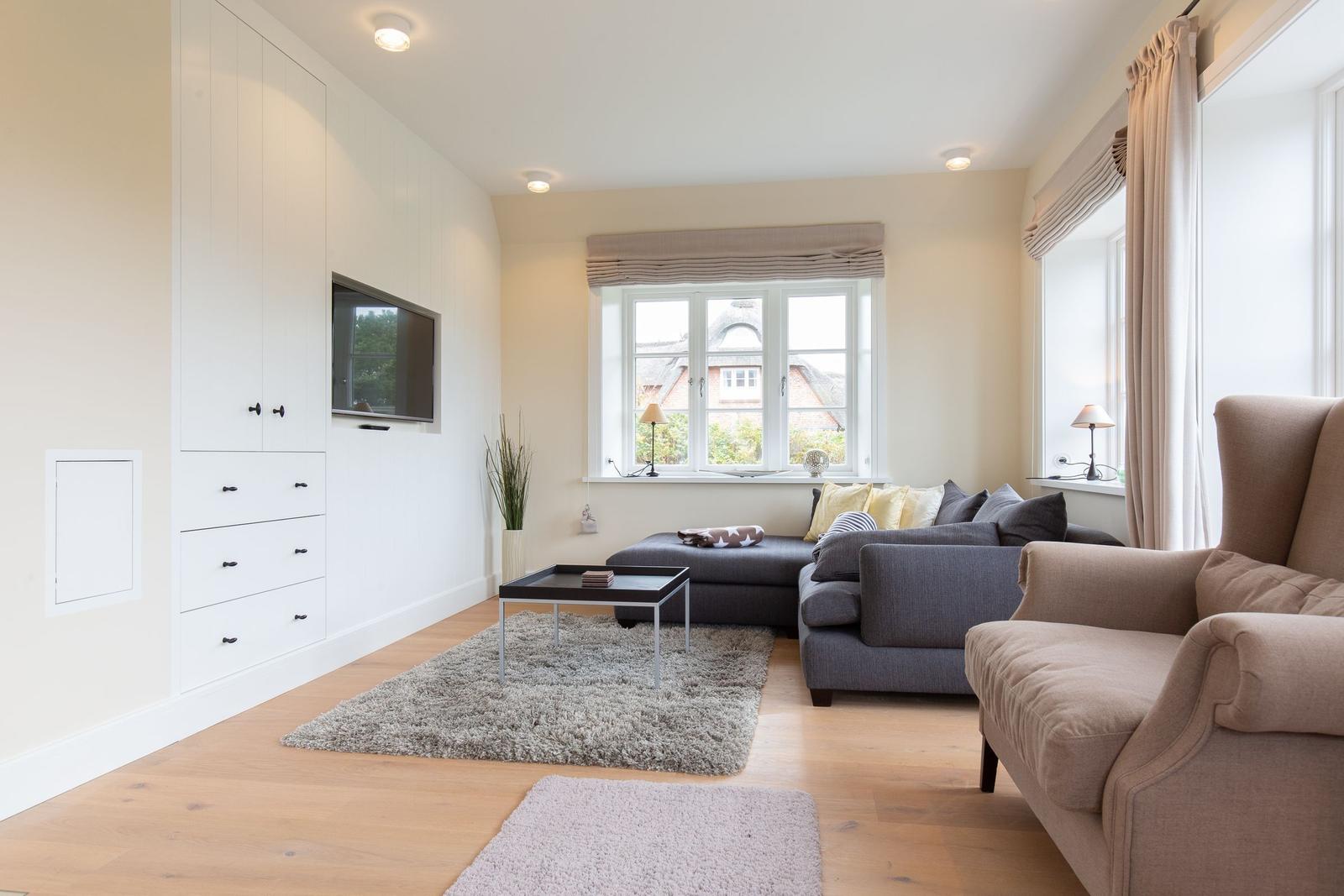 Wohnzimmer mit Sofa, Sessel, TV und Fenstern.