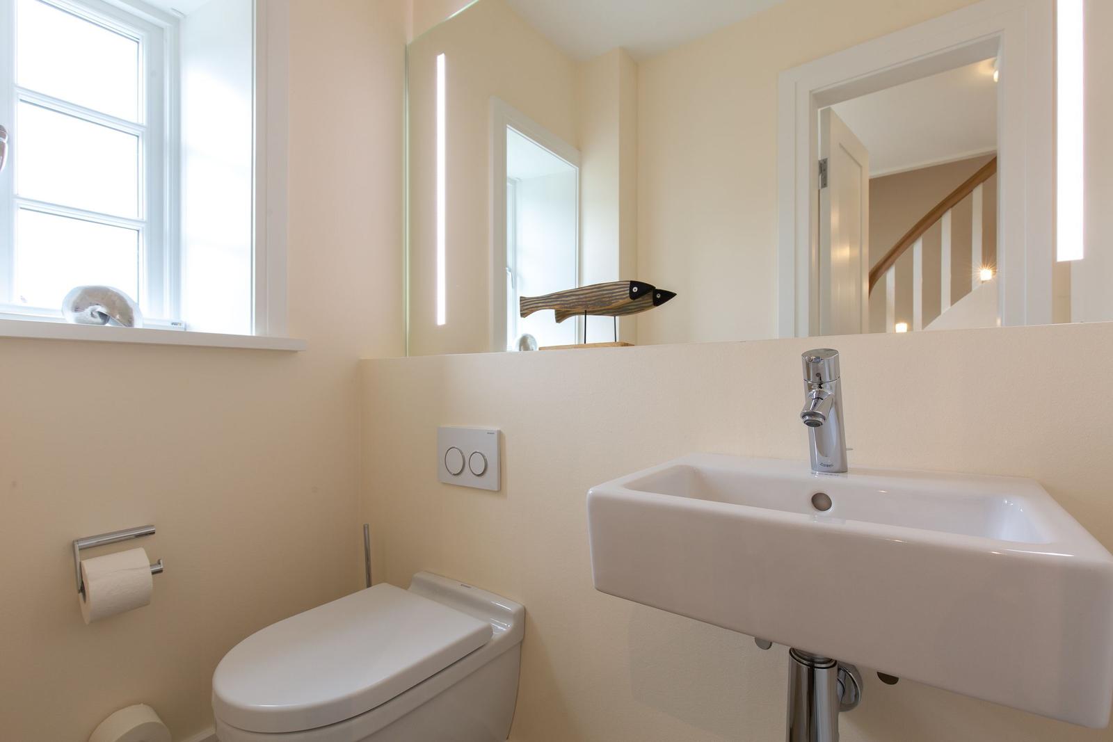 Badezimmer mit Toilette, Waschbecken und Spiegel. Fenster und Holzfigur sichtbar.