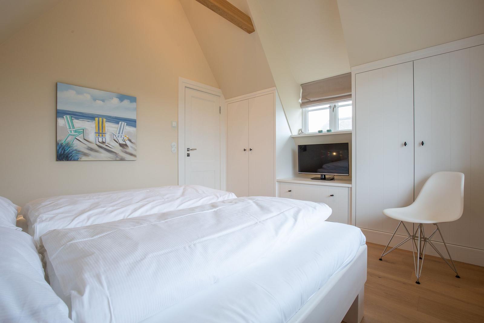 Schlafzimmer mit Doppelbett, Kleiderschrank und Fernseher an der Wand.