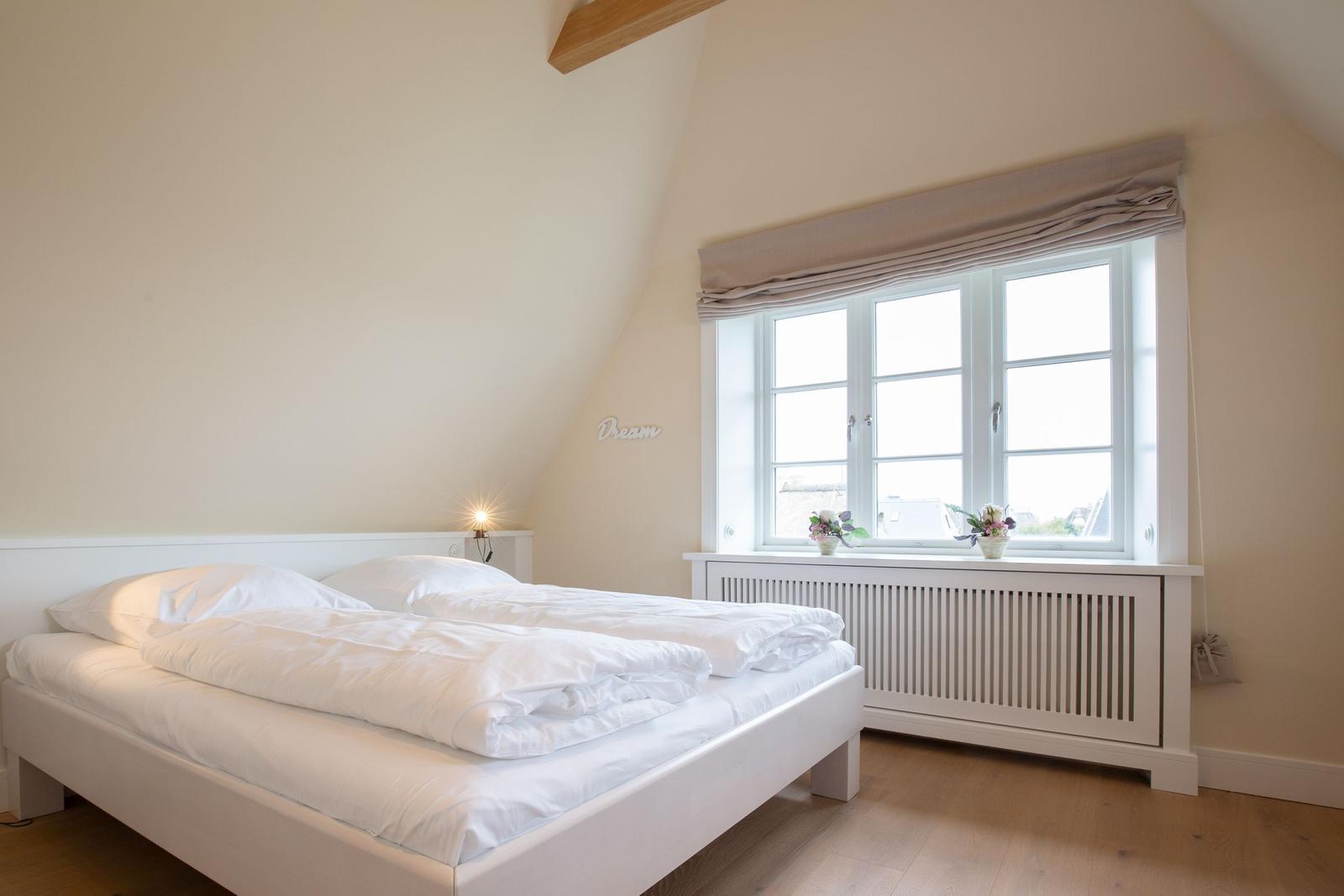 Schlafzimmer mit weißem Bett, Fenster und Holzboden.