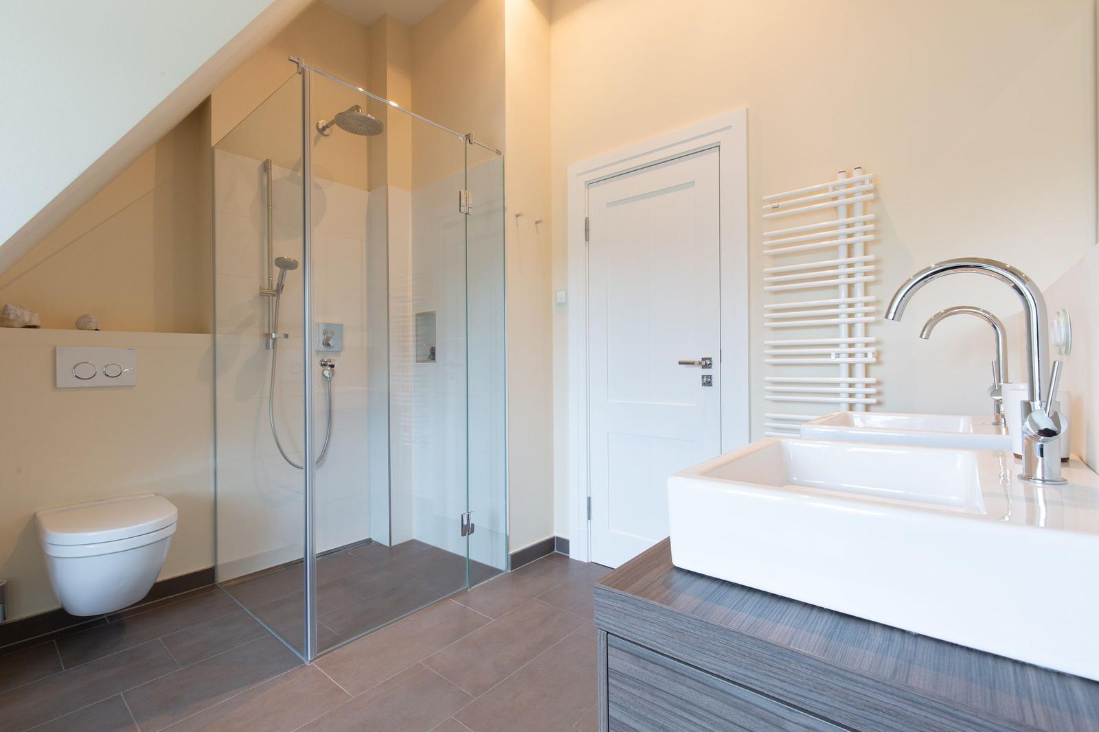 Moderne Dusche mit Glaswand, Waschtisch und Toilette in einem hellen Badezimmer.