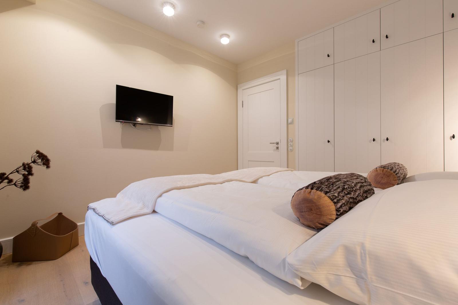 Schlafzimmer mit Bett, Kleiderschrank und Wandfernseher.