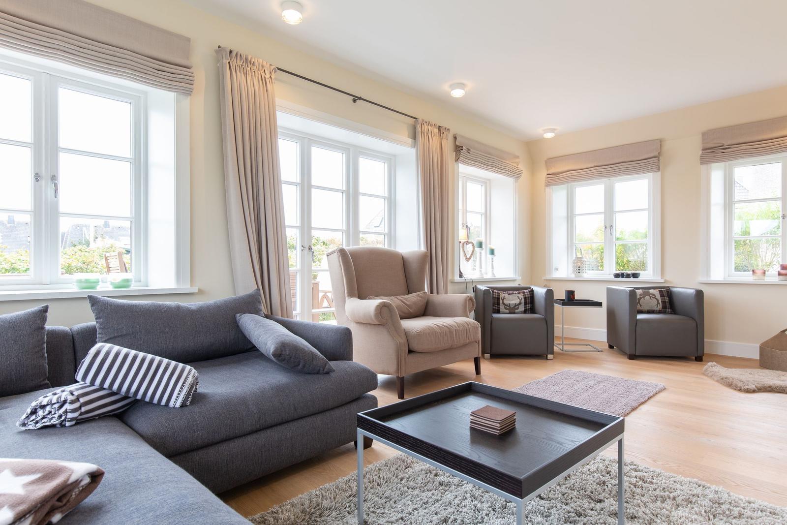 Wohnzimmer mit Sofa, Sesseln und Fenstern mit Vorhängen.