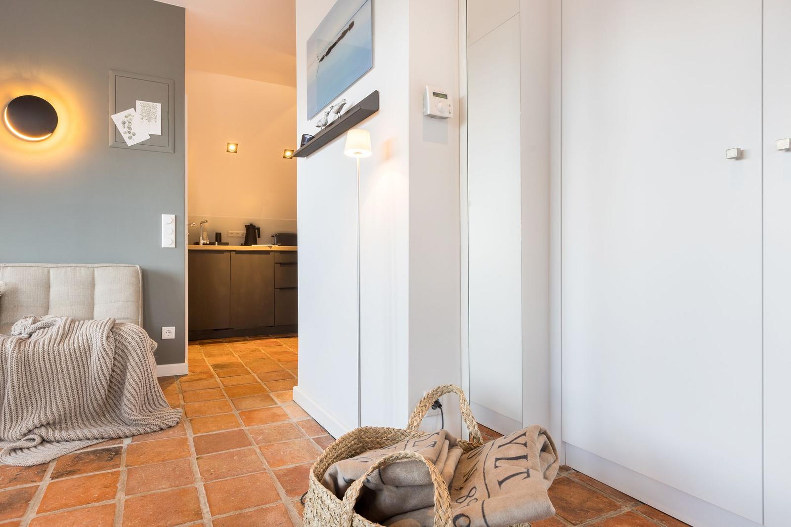 Eingangsbereich mit Schlafzimmer und Küche. Terrakottboden, weiße Schränke und Beleuchtung.