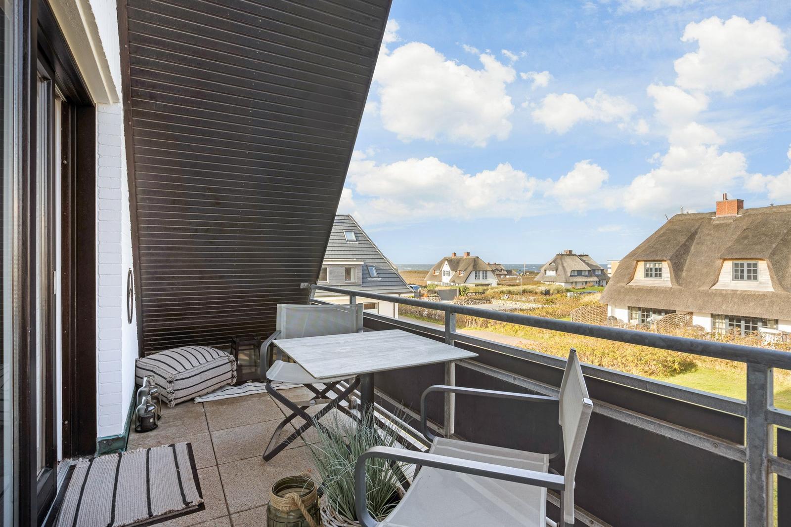 Terrasse mit Tisch und Stühlen, Blick auf Dächer und Meer