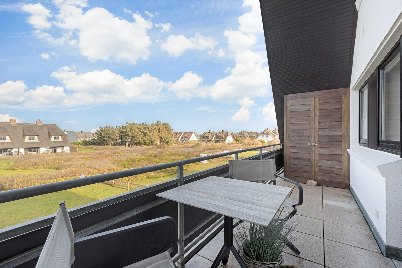 Terrasse mit Tisch und Stühlen. Blick auf Grünfläche und Häuser.