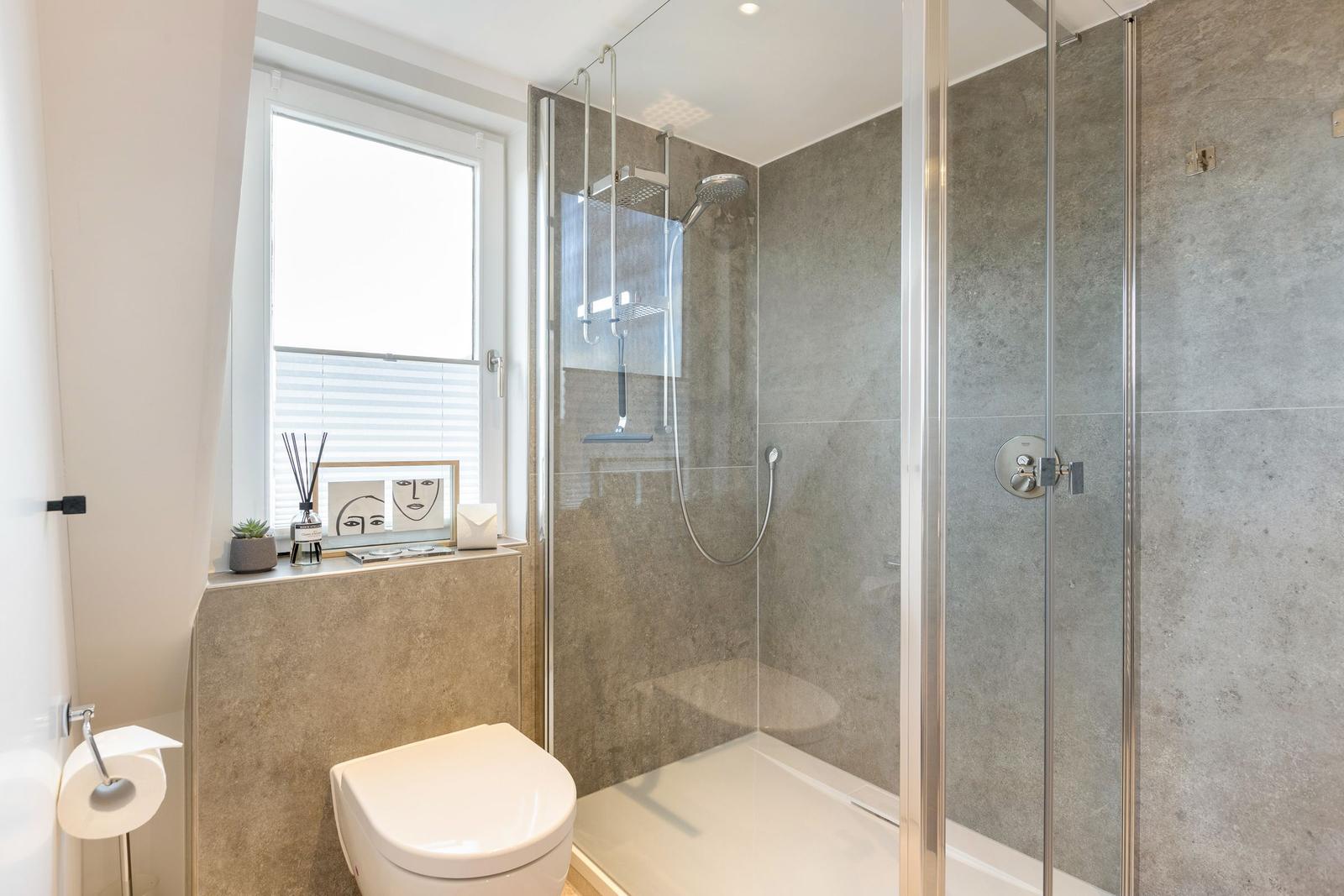 Bad mit Dusche, Toilette und Fenster mit Dekoration.