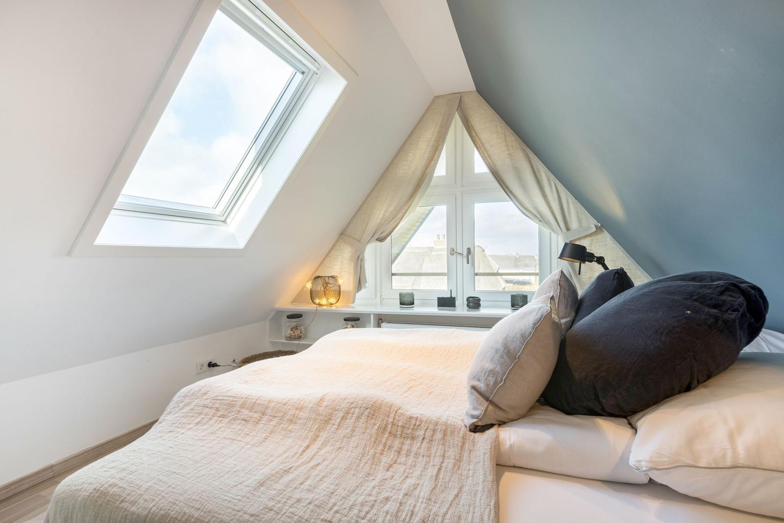 Schlafzimmer mit Dachschrägen, Dachfenster und Fenster mit Vorhängen.