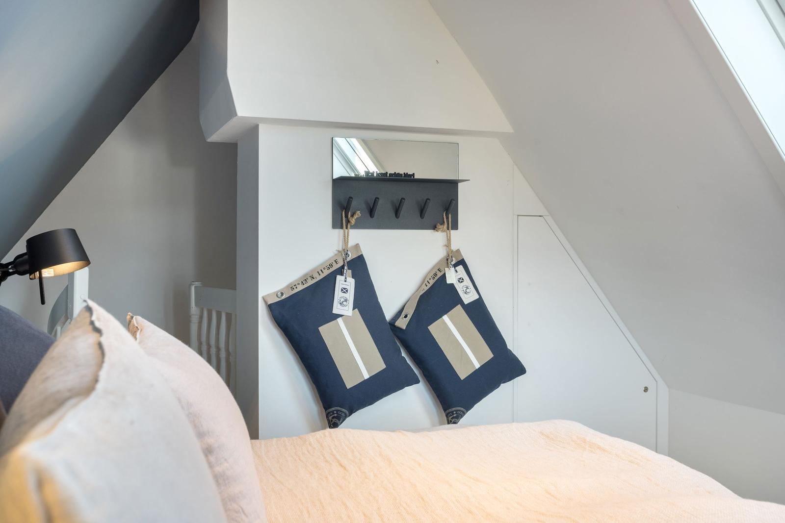 Schlafzimmer mit Dachschrägen, Bett, Wandhalter und Kissen.