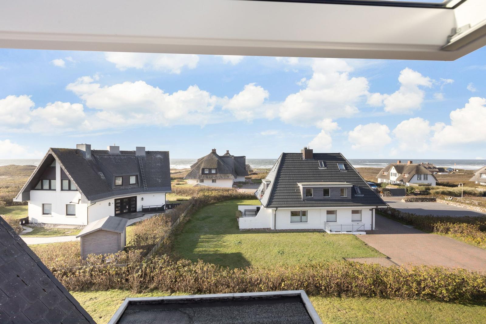 Weitläufiger Blick auf mehrere Häuser mit Dächern und Grünflächen am Strand.