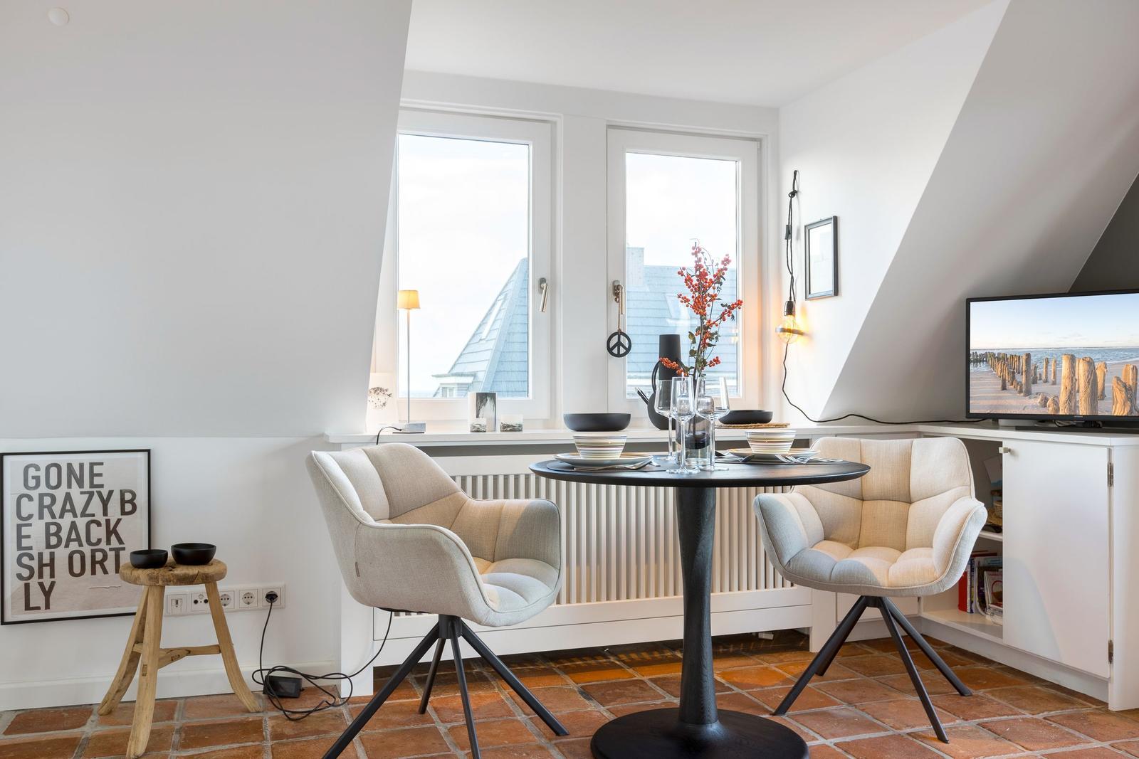 Zimmer mit Esstisch, zwei Stühlen, TV und Fenstern mit Blick.