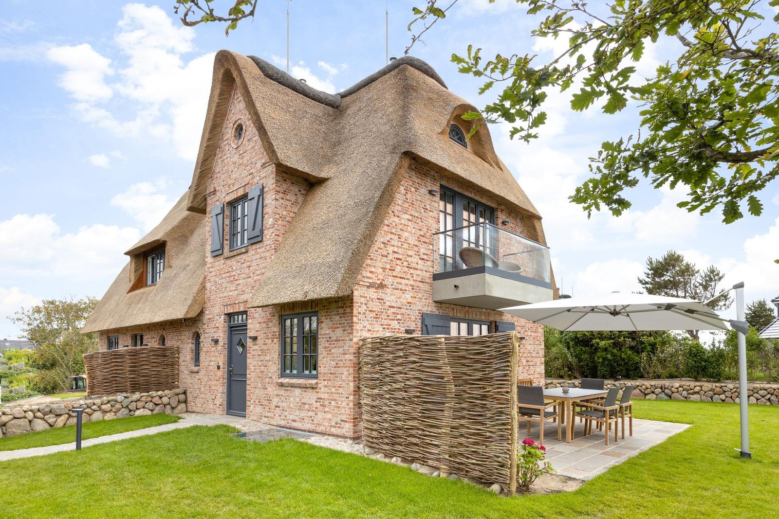 House with thatched roof, garden, and terrace with table and chairs.