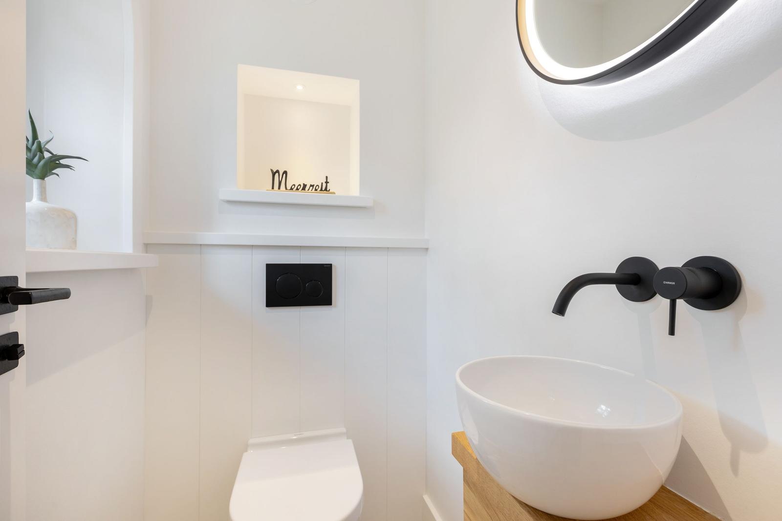 Bathroom with sink, mirror, and toilet. Black fixtures and wooden vanity.