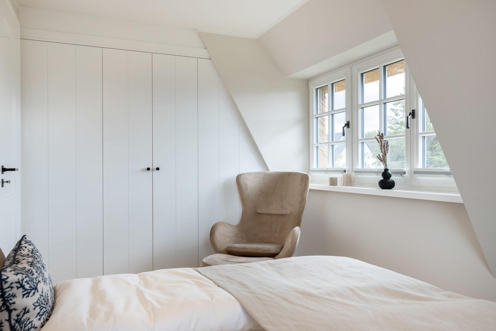 Bedroom with bed, chair, and window. White wall and wardrobe.
