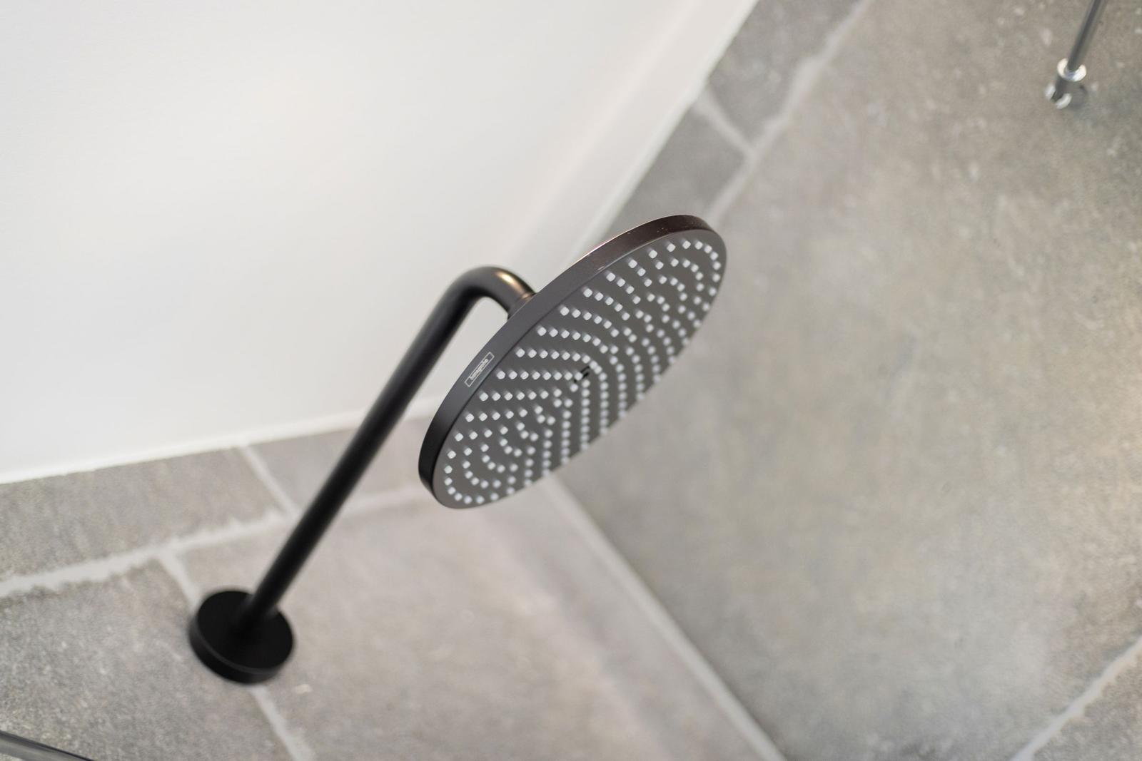 Showerhead with black metal stand on gray tiled floor.